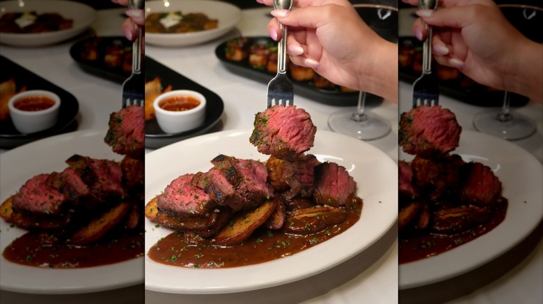 fork stabbed into slice of steak lingering over plate of sliced prime bavette and golden fries