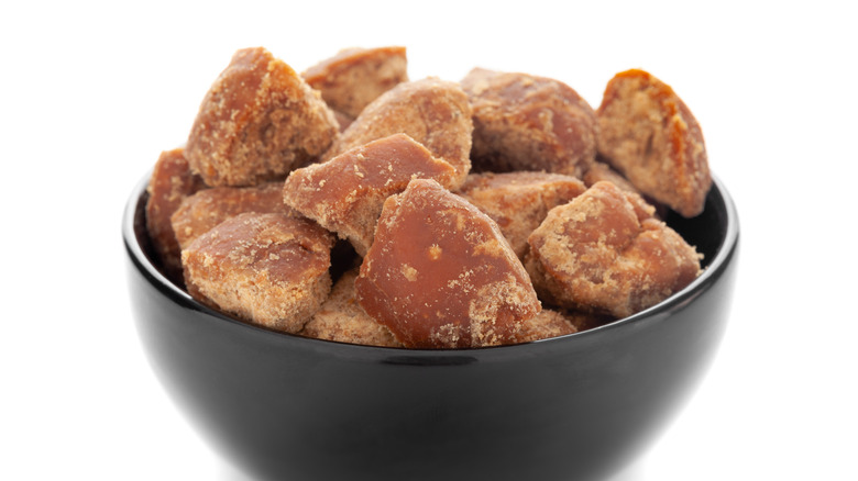 A black bowl of sugarcane jaggery on a white background