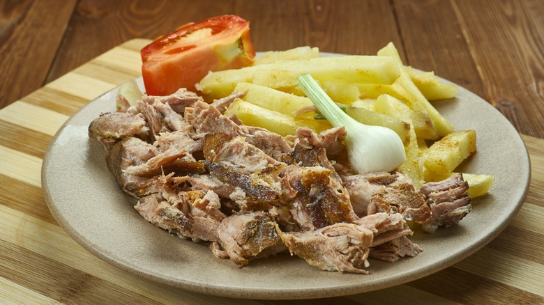 Carolina-Style Barbecue on plate with chopped pork, french fries, tomato wedge, and green onion on wooden choppng board