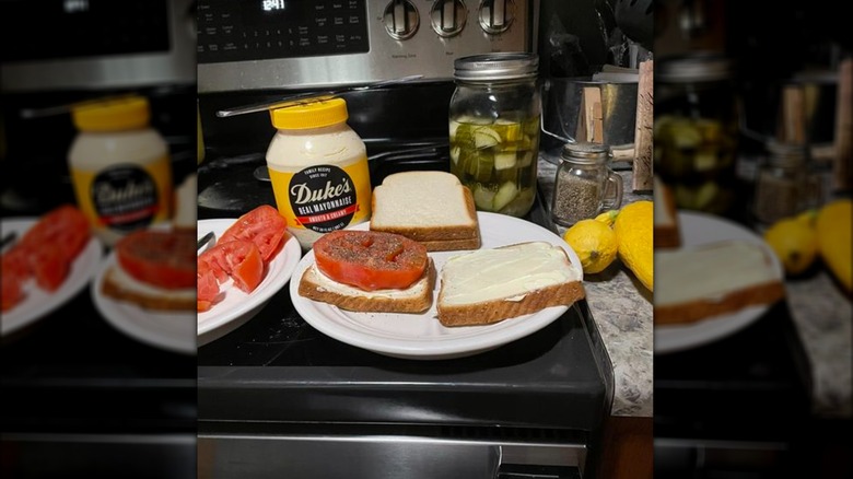 Open face mater sandwich on white bread with Duke's mayo, salt and apper, and jar of pickles in background