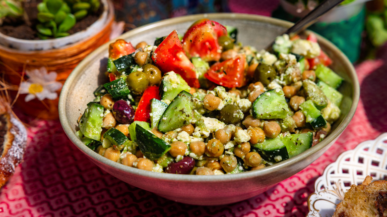 A salad made with chickpeas, diced cucumber, tomatoes, olives, and feta in a ceramic bowl