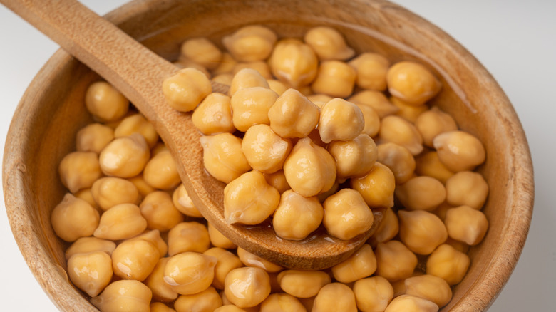Close up of a wooden bowl of plain chickpeas with a wooden spoon
