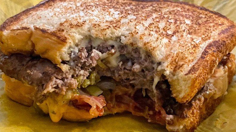 A patty melt with jalapeños and bacon from Whataburger with a bite taken out of it rests on the wrapper