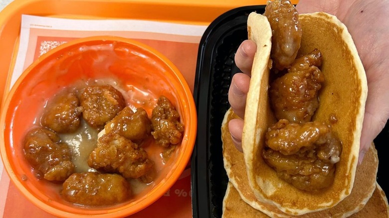 Honey butter WhataWings sit on an orange bowl and a hand is holding a pancake filled with Whatabites