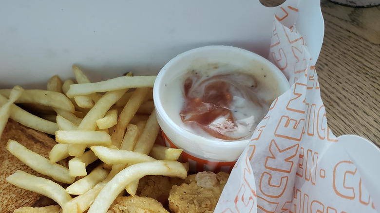 A side of gravy mixed with ketchup sits in the corner of a Whataburger to-go box of fries and chicken