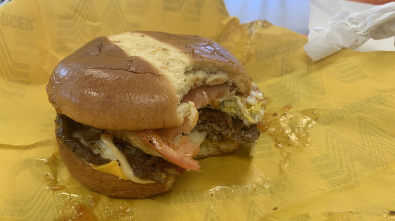 A burger featuring a brioche bun from Whataburger with a bite taken out of it rests on the wrapper