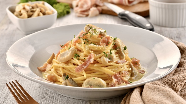 Spaghetti Carbonara with mushroom and fork served in dish isolated on wooden table side view of italian fast food