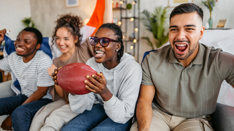 A group of friends watching a TV off-camera, one holding a football