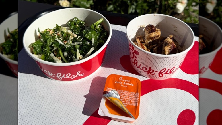 Chick-fil-A grilled nuggets and kale crunch salad in to-go cups on a table next to a packet of Zesty Buffalo sauce
