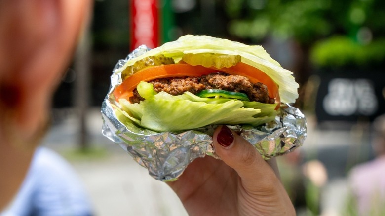 Person holding a five guys lettuce wrapped burger wrapped in foil