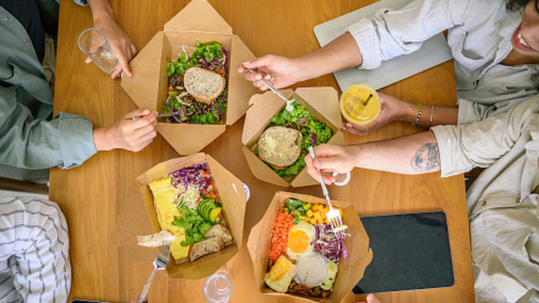 People eating salads and grain bowls in to-go containers at a fast food restaurant
