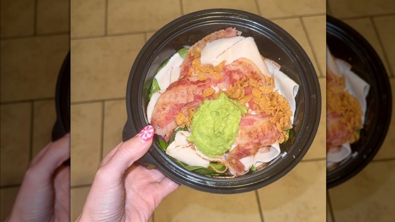 Person holding a subway turkey protein bowl in a black, plastic to-go container