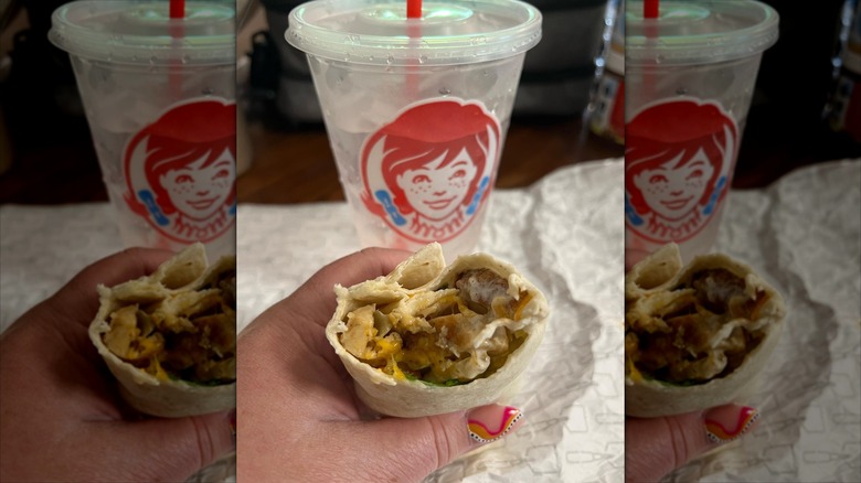 Person holding Wendy's Grilled Chicken Wrap with a plastic to-go cup of water in the background