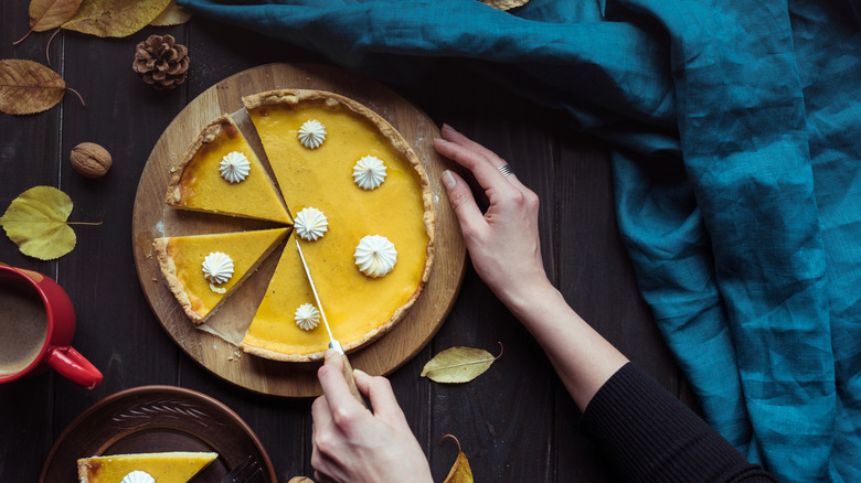 hands cutting a pumpkin pie