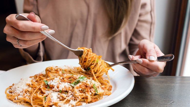 Person swirling spaghetti Bolognese around a fork with a spoon