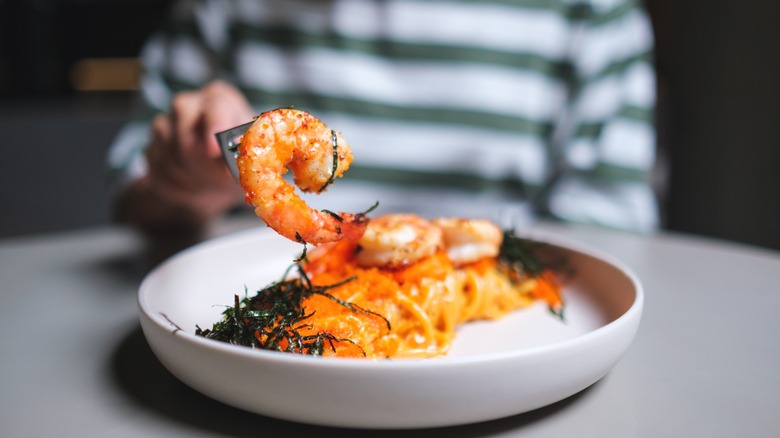 Closeup image of a person eating spicy shrimp spaghetti in a white bowl