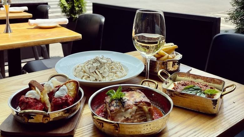 Various dishes, like lasagna, pasta with truffles, French fries, and a glass of wine at outdoor patio dining table at Osteria Nonnino