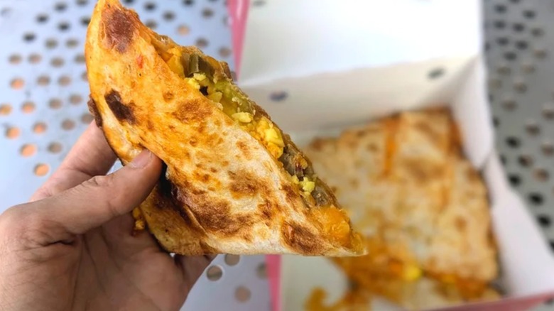 A hand holding half a Sheetz breakfast quesadilla over the other half in the box