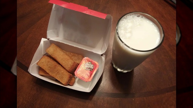A box of Sheetz French toast sticks with a container of syrup next to a glass of milk