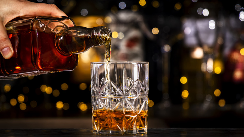 Bartender pours bourbon or whiskey in glass.