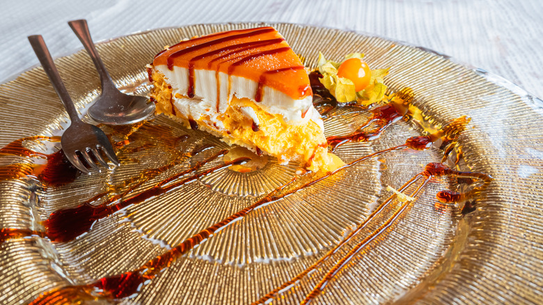 A slice of Spanish whiskey cheesecake on a glass platter with a drizzle of caramel