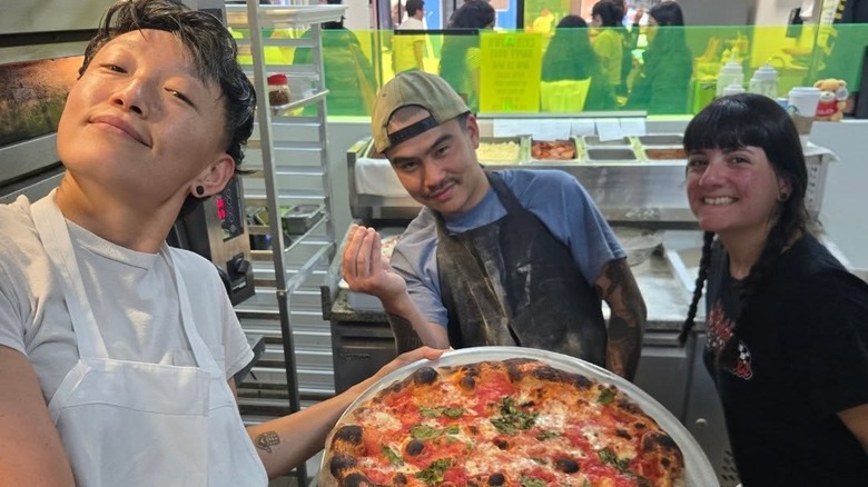 Pizzeria employees holding up pizza