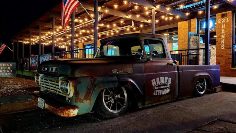 Hanks Chop Shop exterior at night with old fashioned car parked in front with company name written on it and American Flag flying in background