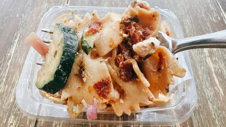 Whole Foods bistro pasta salad on fork with the container in the background on a wooden table