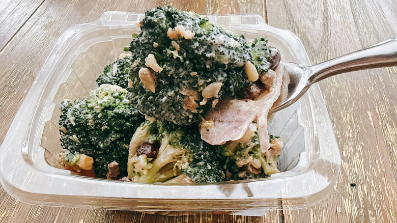 Whole Foods Broccoli crunch with bacon on fork with the container in the background on a wooden table