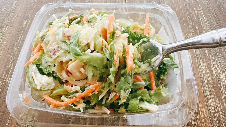 Whole Foods spinach feta orzo on a fork with the container in the background on a wooden table