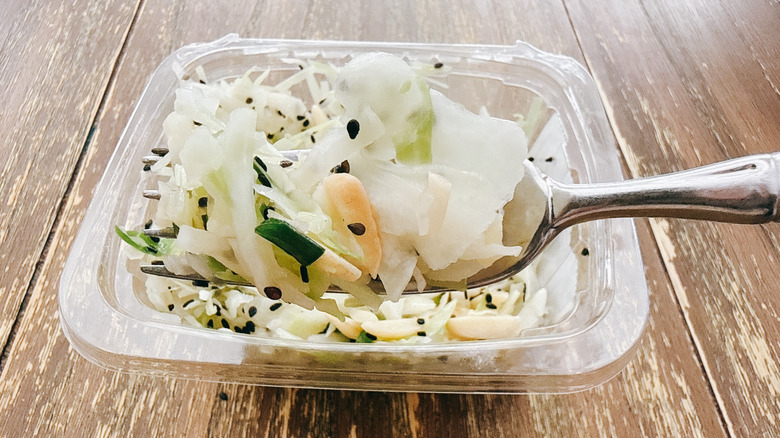 Whole Foods cabbage crunch salad on fork with the container in the background on a wooden table