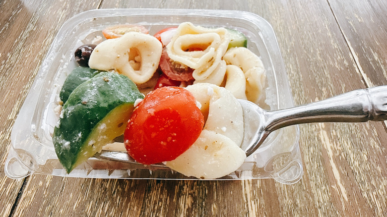 Whole Foods greek tortellini salad on fork with the container in the background on a wooden table