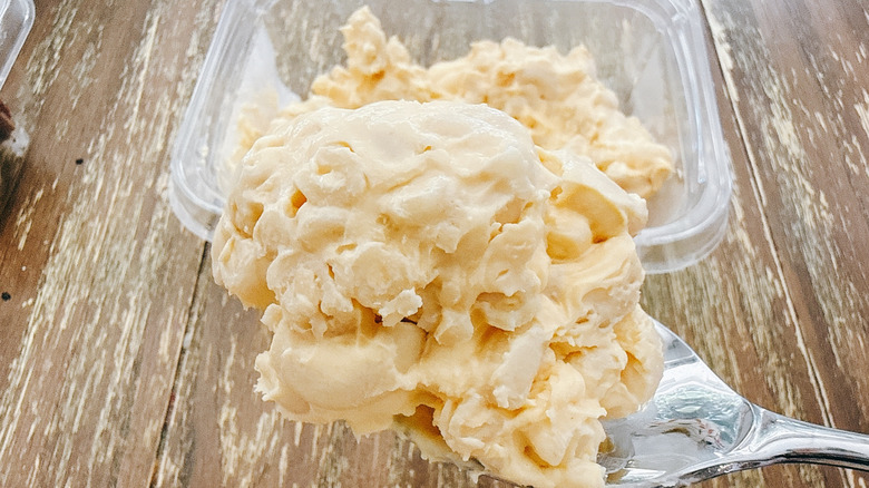 Spoonful of Whole Foods mac and cheese with the container in the background on a wooden table