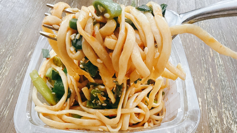 Whole Foods sesame cucumber noodles on fork with the container in the background on a wooden table