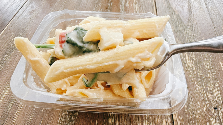 Whole Foods Smoked Mozzarella Pasta Salad on fork with the container in the background on a wooden table