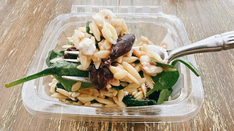 Whole Foods spinach feta orzo on fork with the container in the background on a wooden table
