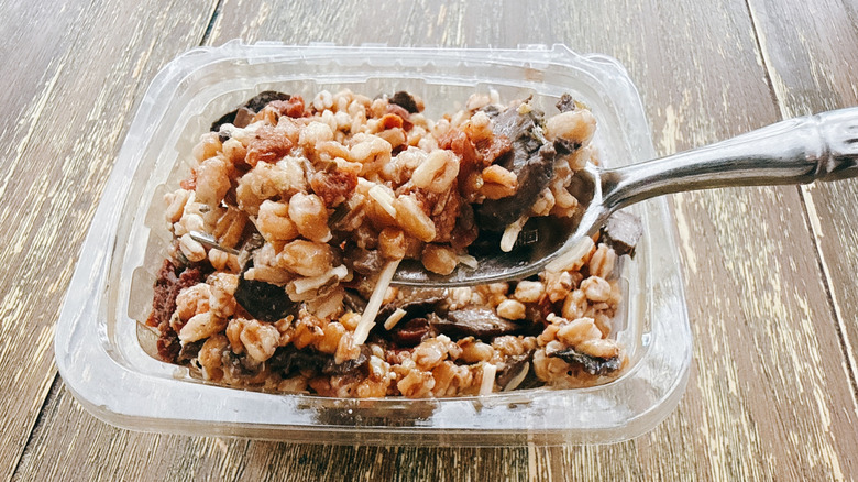 Whole Foods Tuscan farro on fork with the container in the background on a wooden table