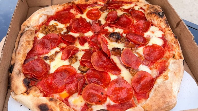 A whole Neapolitan-style pizza with red sauce, fresh mozzarella, sausage, and pepperoni, set in a pizza box