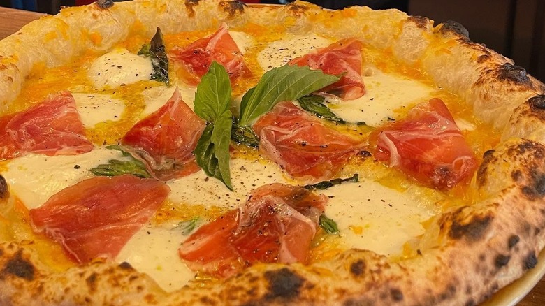 Close-up of a whole Neapolitan-style pizza with yellow tomato sauce topped with capicola, fresh mozzarella, and basil leaves