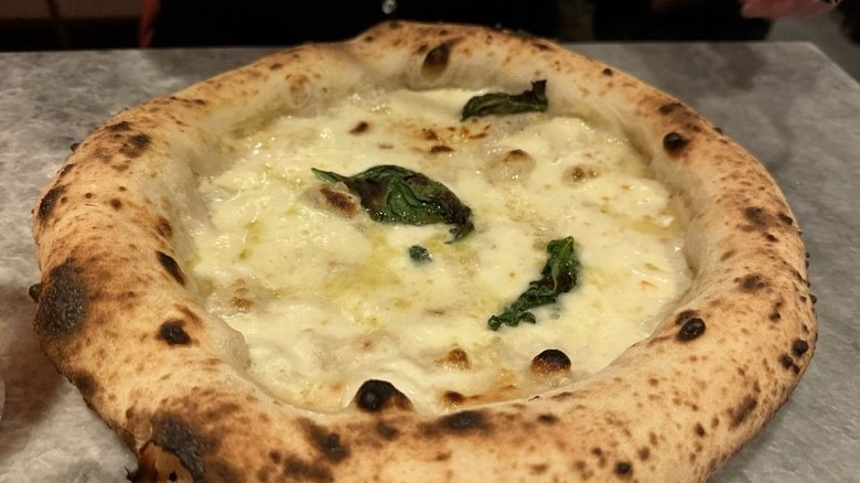 A whole Neapolitan-style bianca pizza topped with three basil leaves set on a gray marble counter