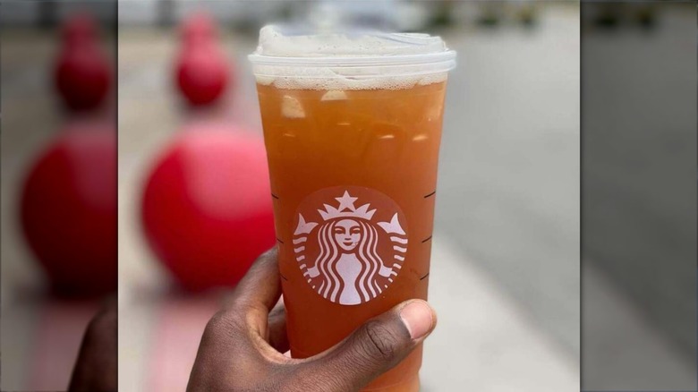 A hand holds an iced black tea from Starbucks