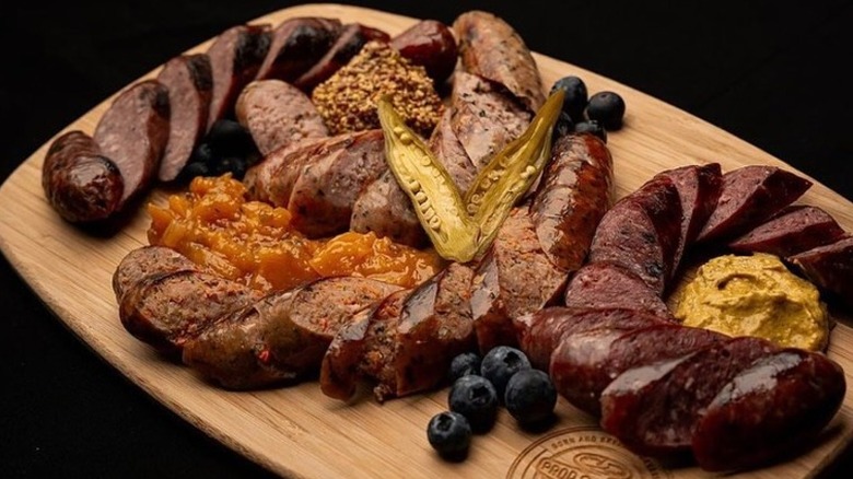 sliced, smoked sausage on a board with mustard, blueberries, and pickled okra