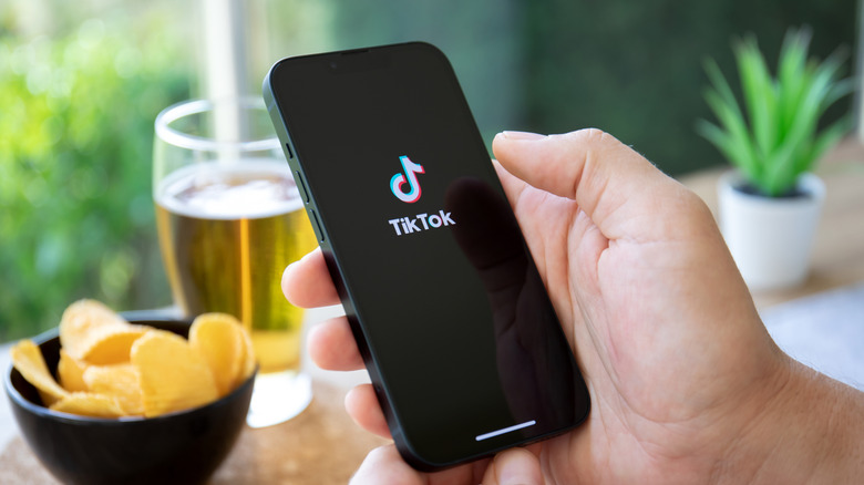 peron holding phone with TikTok app in front of beer and potato chips