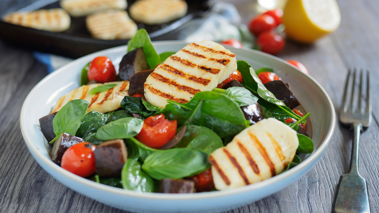 Spinach salad topped with grilled halloumi in a white bowl