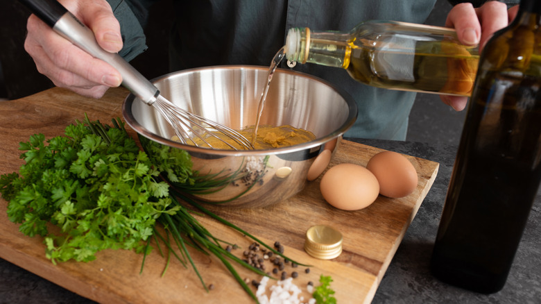 Person whisking together a homemade salad dressing in a metal bowl made with oil, eggs, and fresh herbs