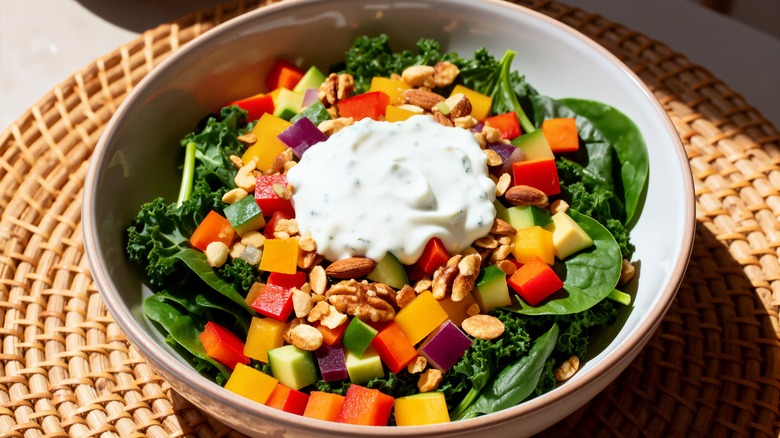 Salad with diced vegetables, nuts, seeds, and white dressing in a tan-colored bowl set on a wicker place mat