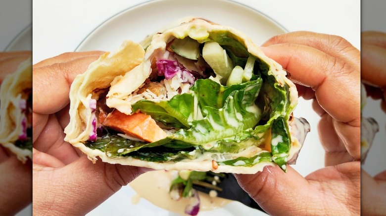 Hands holding salad wrap over a white plate