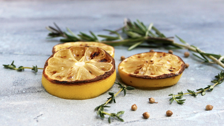 Sliced, charred lemons surrounded by fresh rosemary and thyme sprigs