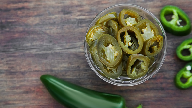 Fresh and pickled jalapeños in a glass ramekin on a wood table