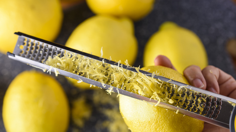 Lemon zest on a microplane grater with lemons in the background